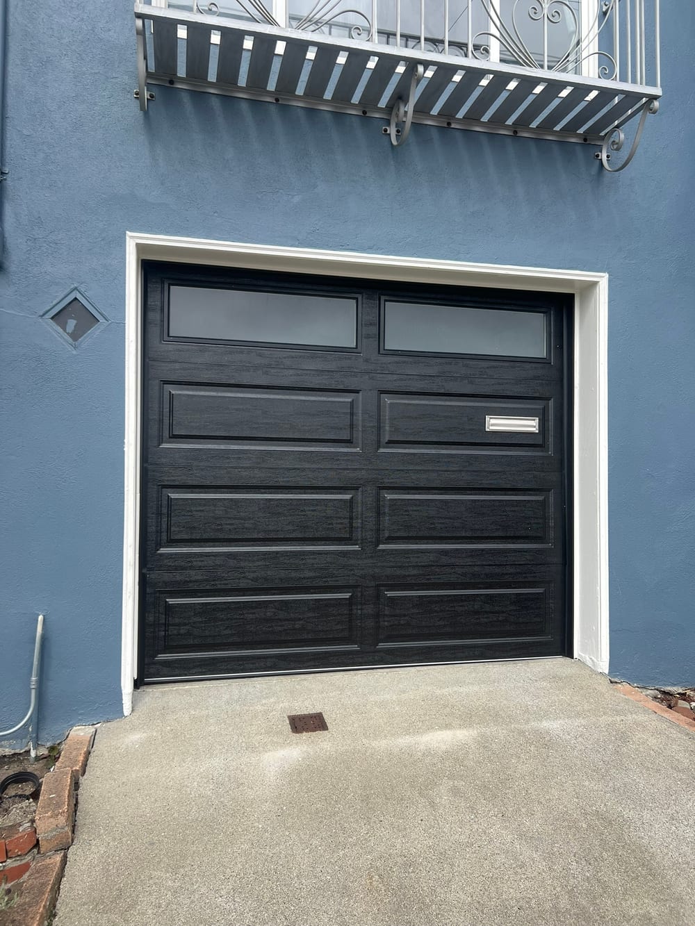 Black flush garage door with a window row, newly fitted in a blue stucco wall