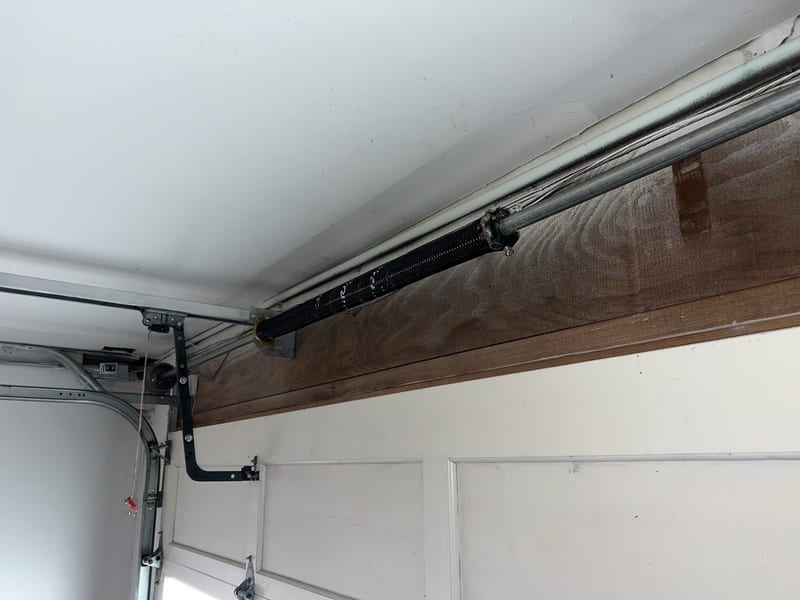 Newly fitted torsion spring on the bar above a white sectional garage door
